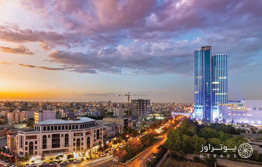 برج آرمیتاژ مشهد در غروب خورشید از فاصله دور که نمایی از خیابان و ساختمان‌ها و دیده می‌شود.